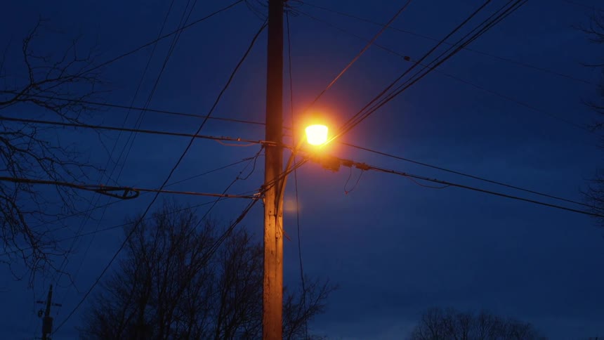 A utility pole with a streetlight with trees the sky and clouds in the background