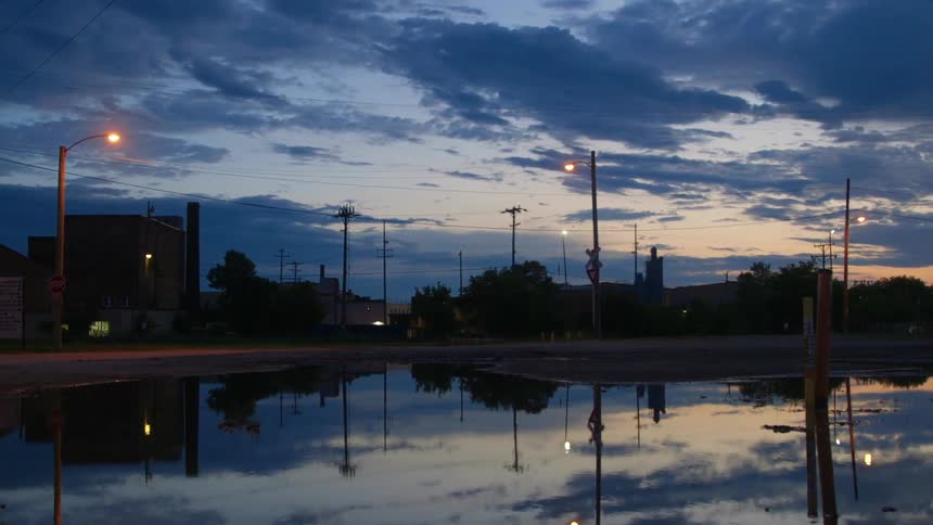 A neighborhood with buildings and streetlights with the sky and clouds in the background