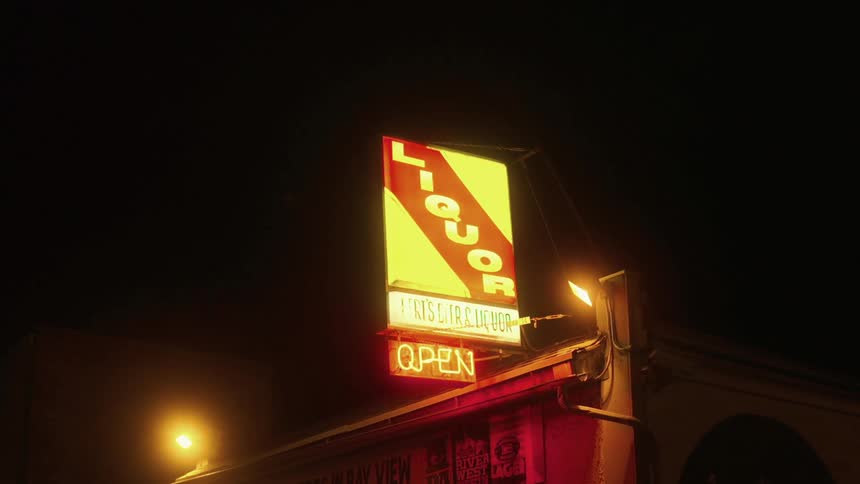 Sign about liquor sits above open neon sign on roof of building at night