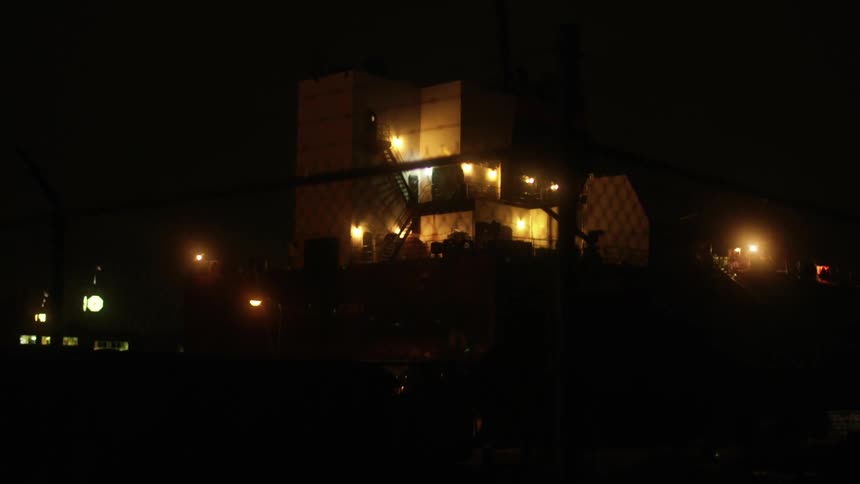 A fence with barbed wire with a building and light in the background