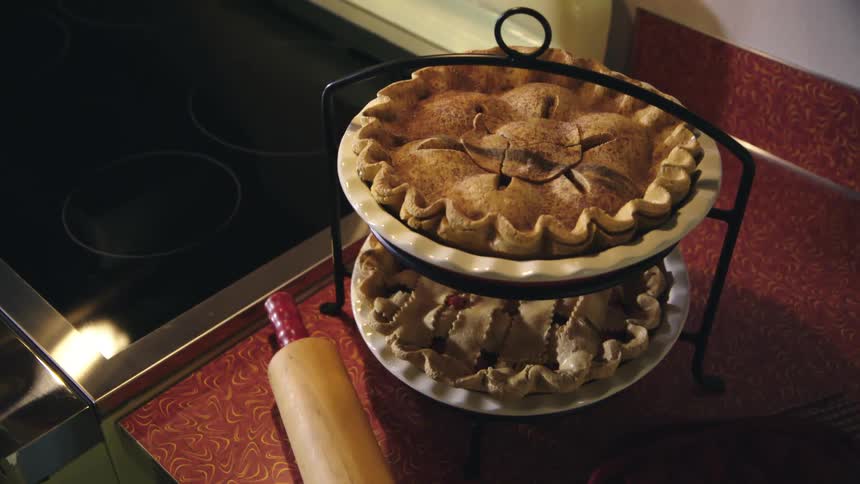 Two homemade pies sit on a cake stand on a kitchen counter