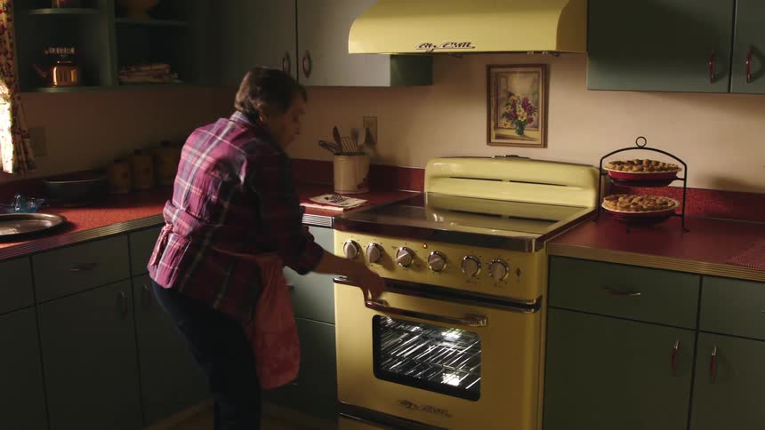 A woman gets up from her kitchen table to check on muffins in the oven