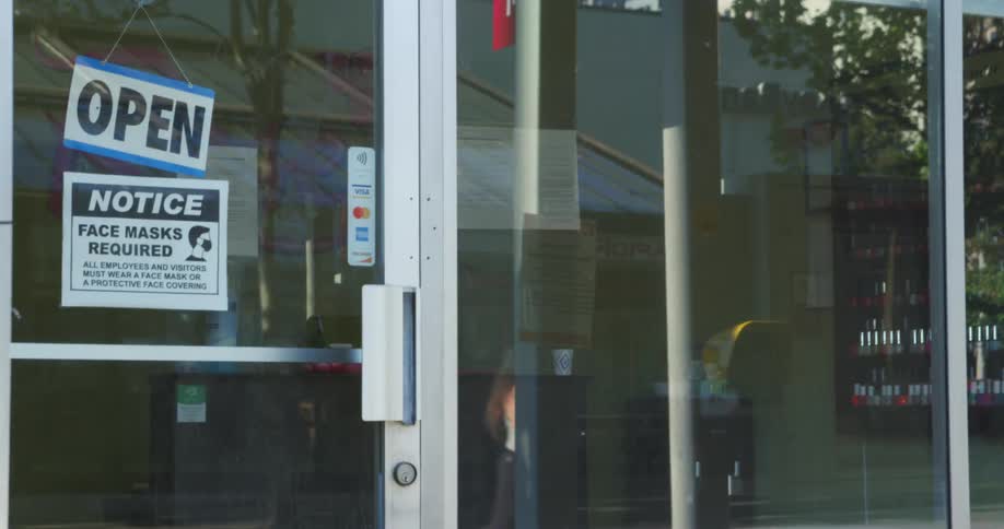 A store window and door with signs with a reflection of a woman walking