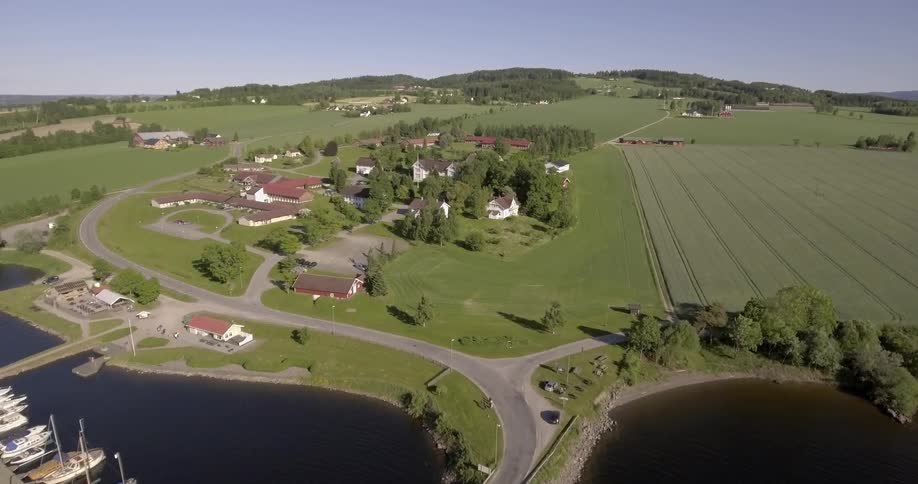 Aerial view of some homes and boats docked by the water with fields in the distance