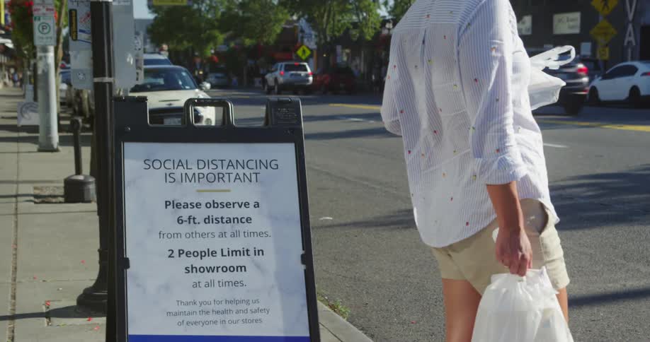 A person standing on a sidewalk next to a city street holding two plastic bags