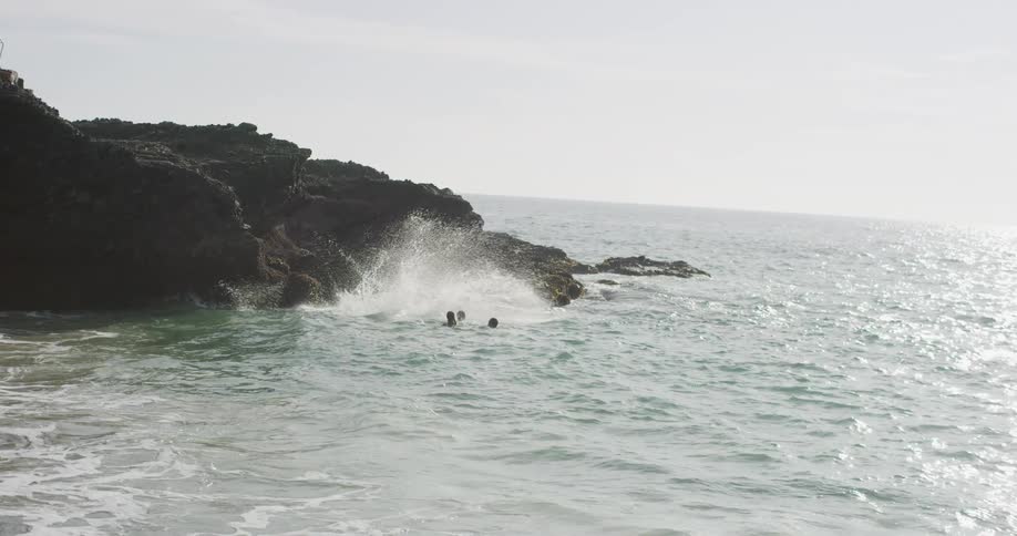 Guy and a girl cliff jumping into the ocean with friends