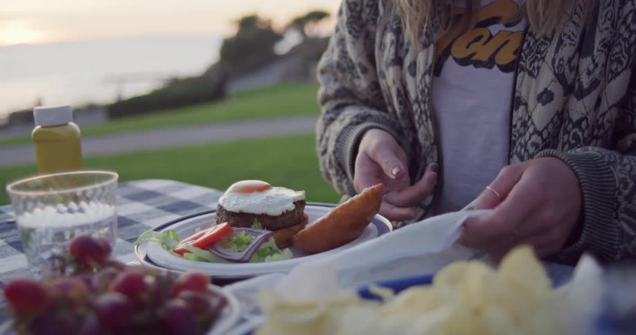 A woman sitting at a table with food with the sky and clouds in the background