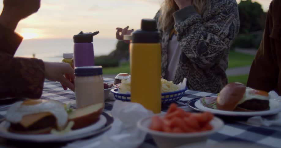 Sun on horizon tints sky red as people sit at picnic table eating hamburgers