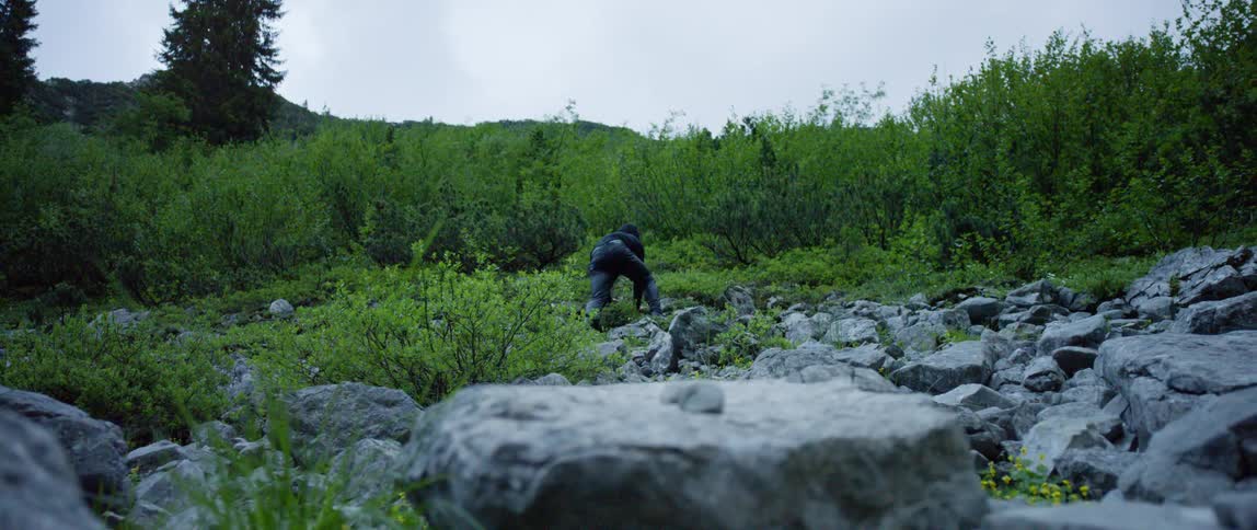 A man climbs a rocky hill in the wilderness on his hands and feet on a cloudy day