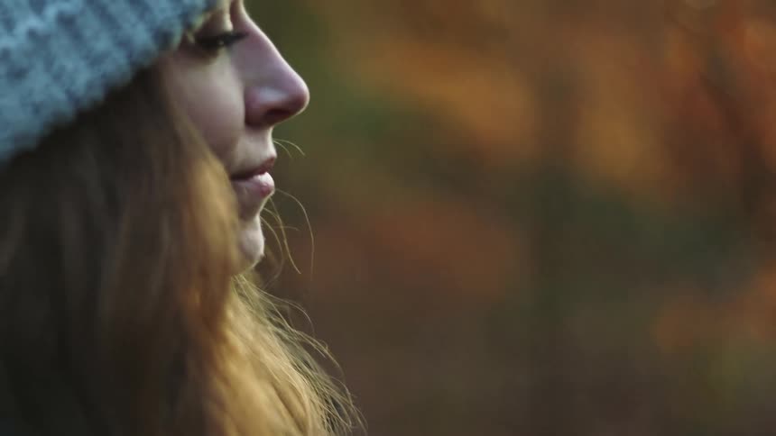Woman wearing knit hat stands outside against fall colors