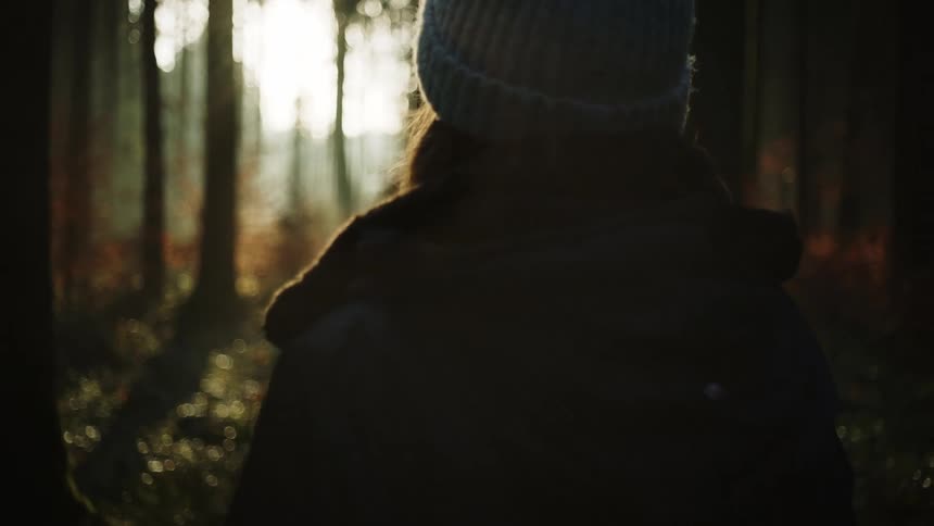 A woman in cold weather clothing stands in a woodland on a cold day