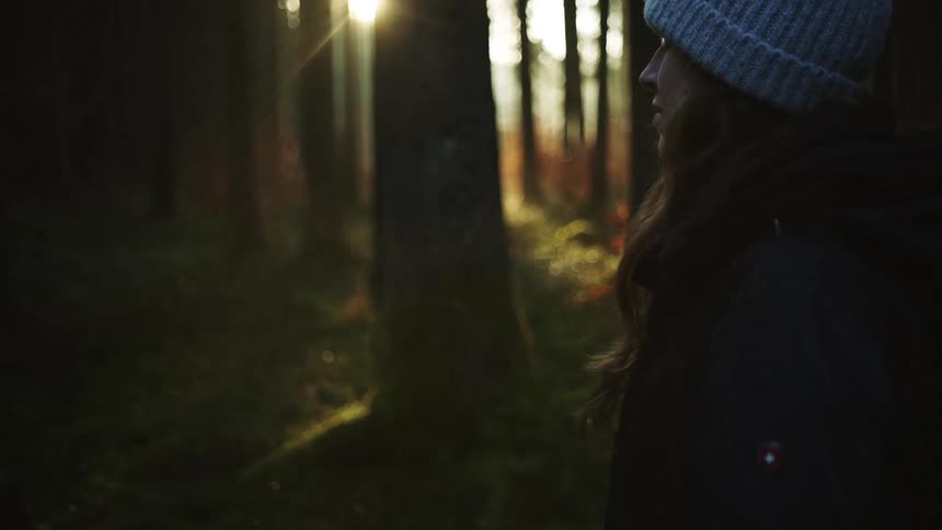 A woman is standing outdoors in the woods at dusk