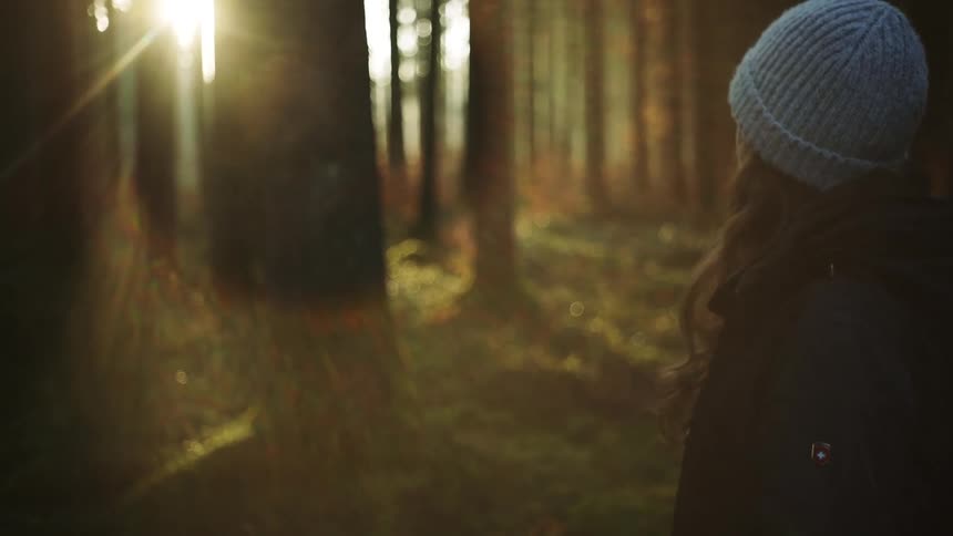 Young woman in cold forest with morning sun shining through trees