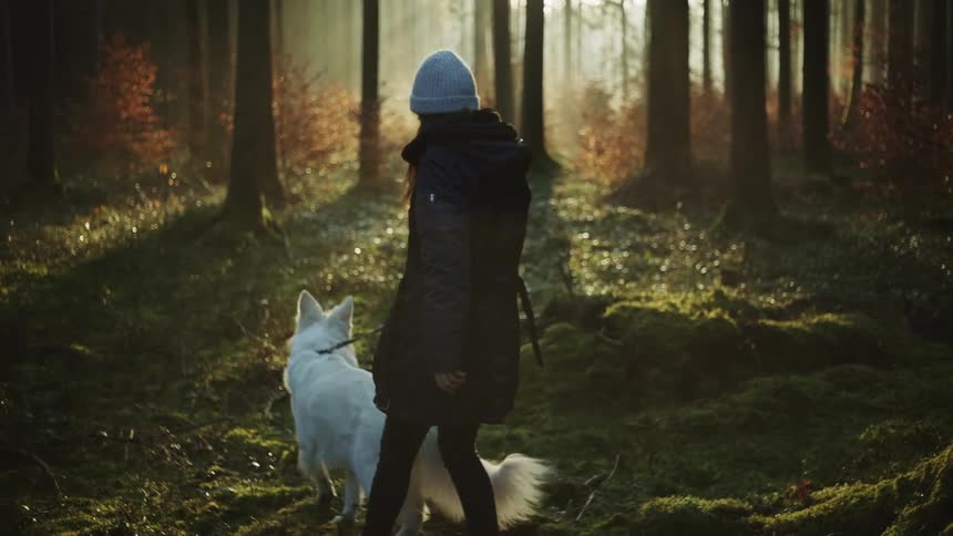 A woman walks through a heavily wooded area with a dog