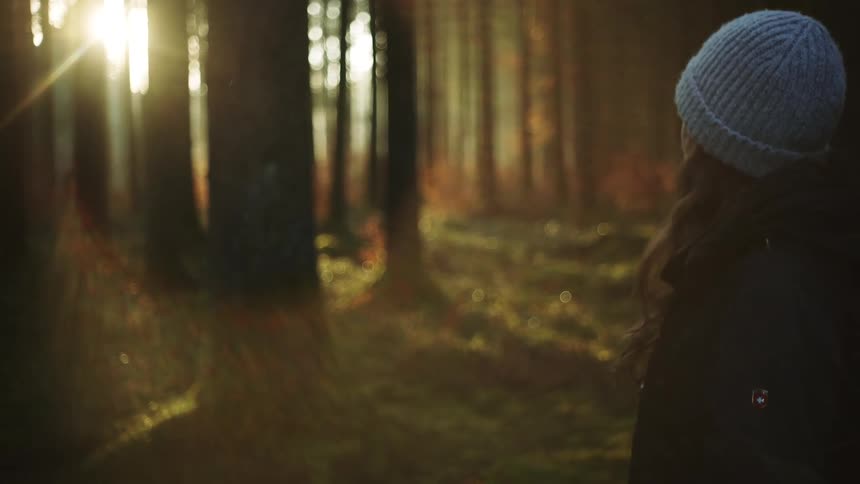 A woman is standing in the forest at dusk