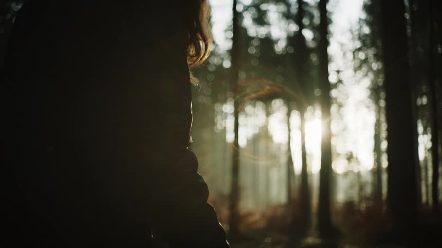 A woman pets a dog while standing in a forest during the day