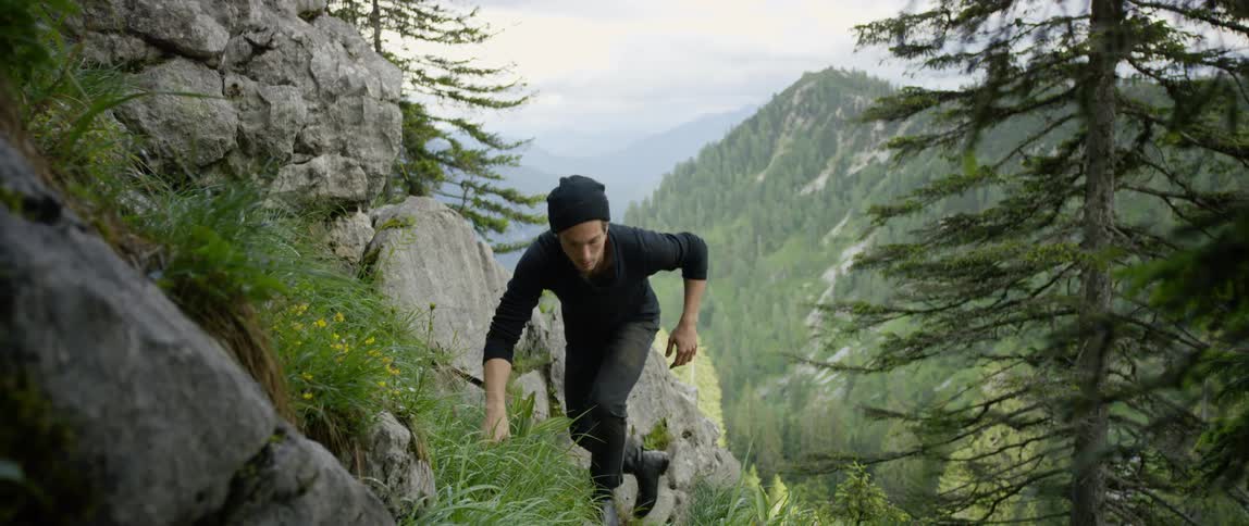 A man climbs a steep stone covered mountain slope during the day