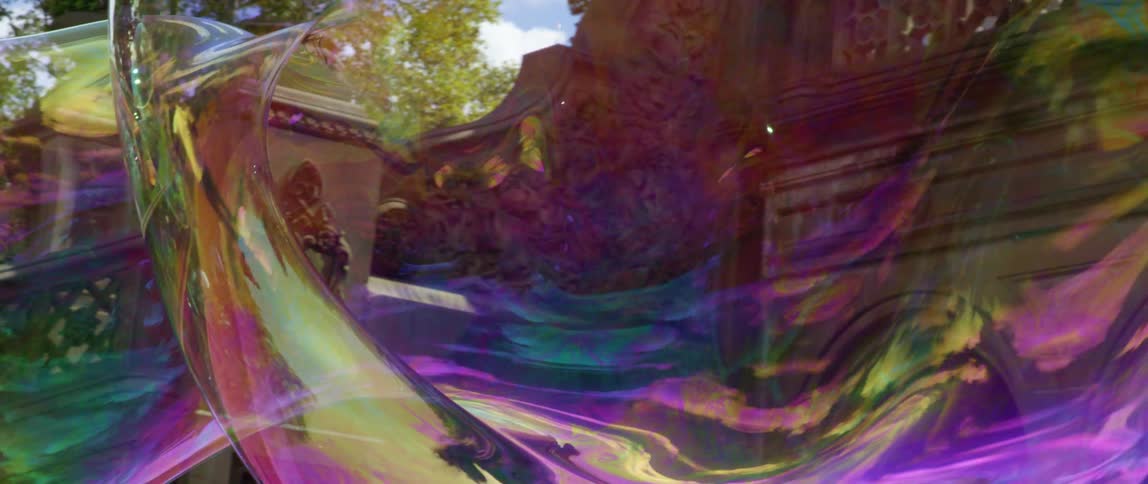 A large bubble floats through a park then bursts