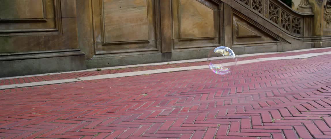 A bubble floating and popping above a brick sidewalk