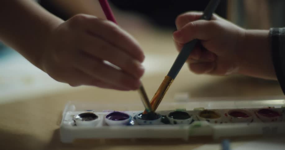 Two kids dab paint brushes into same color on watercolor paint tray
