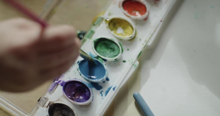Two kids paint with small brushes and water color palette on large sheet of paper