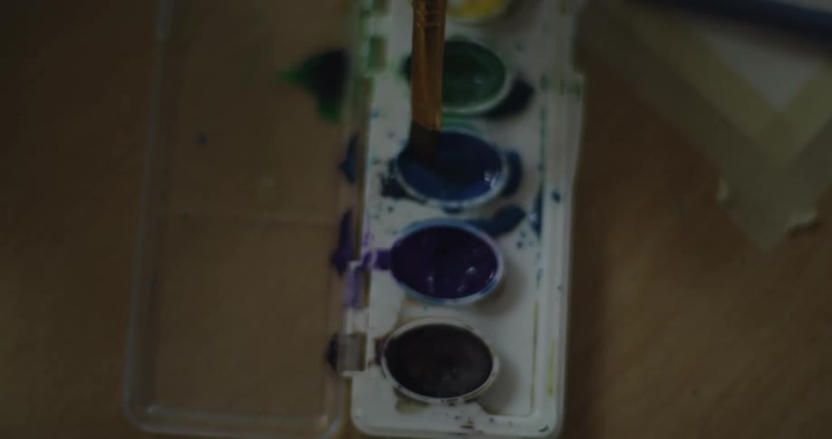 A person dipping paint brushes into paint