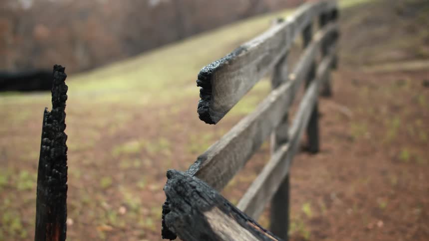 The burned section of a wooden fence in the hills during the day