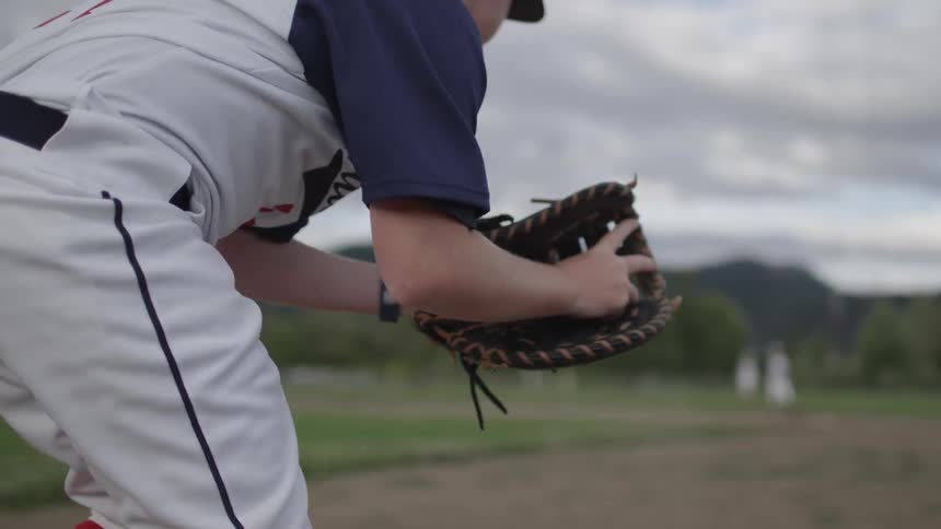 A boy in a baseball uniform catches and then throws a baseball