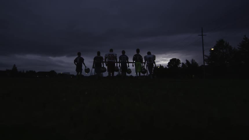 Six young men walking into the sunset while wearing their football uniforms