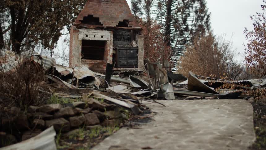 Debris occupies area near ruined house surrounded by conifer trees