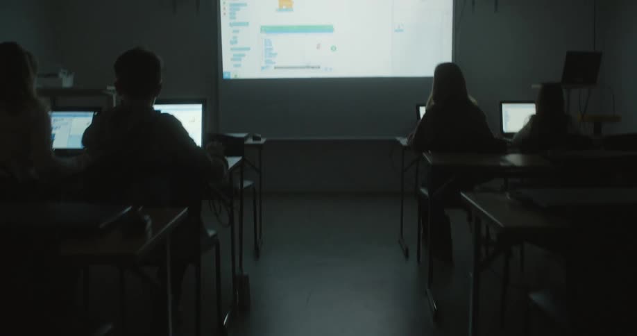 People sitting in a dark classroom with laptops and a projection screen