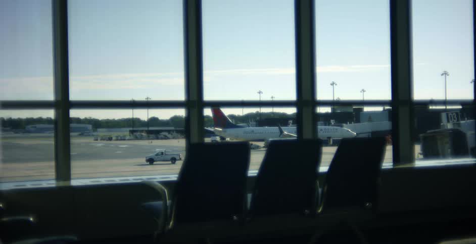 Truck can be seen from windows in terminal waiting area driving across tarmac away from parked airplane