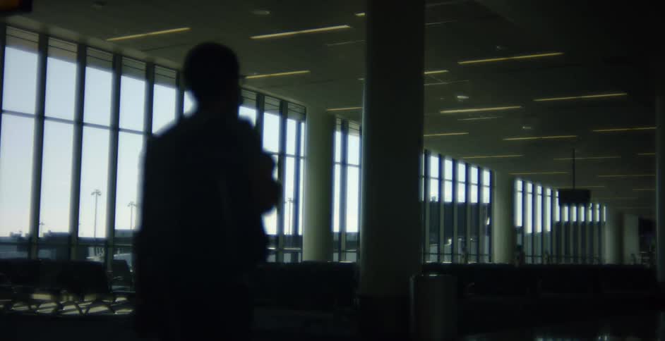 People wearing face mask and silhouetted by light from windows walks into airport waiting area