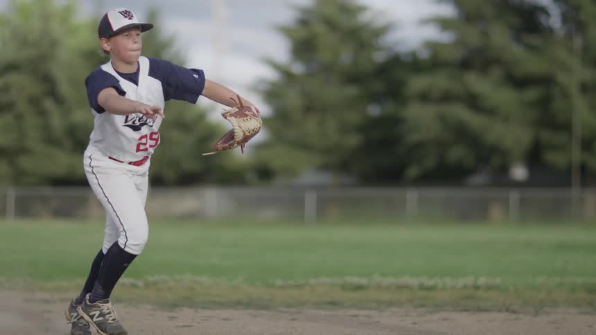 A boy catches a ground ball and tosses it to another player