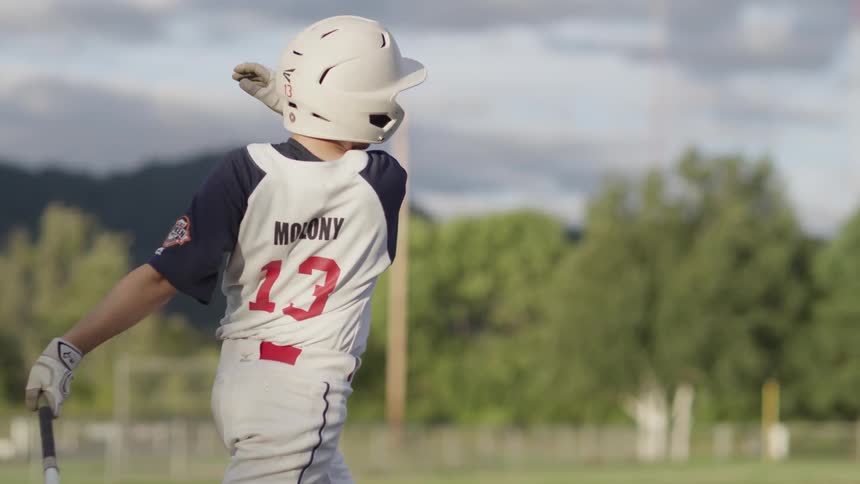 Boy in baseball jersey swinging a bat and hitting a baseball