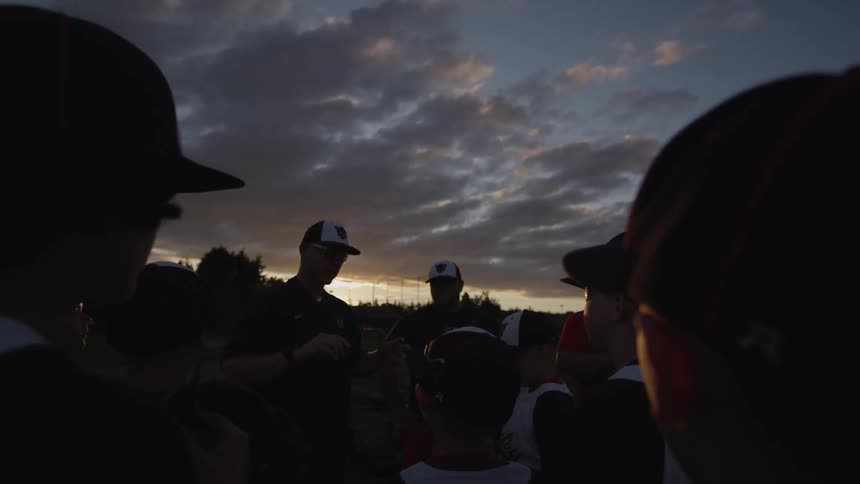 Baseball players and coaches standing in a group as one of the coaches speaks
