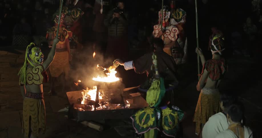 Costumed people are putting things in a flame at night