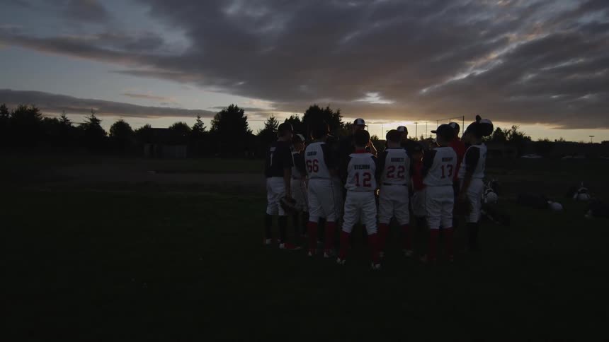 Boys in baseball jerseys standing with coach on field at sunset