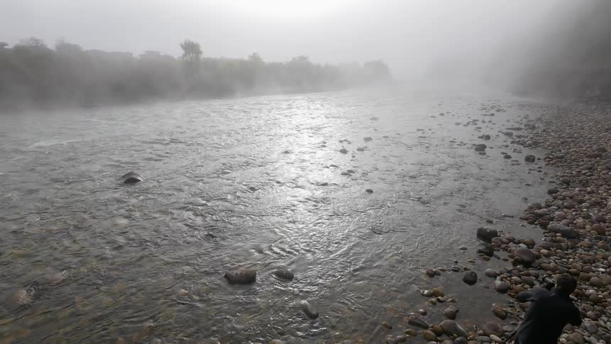 A man is photographing a stream as heavy rain drops down