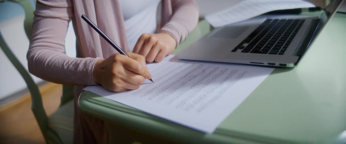 Woman sitting at desk writes music next to open laptop