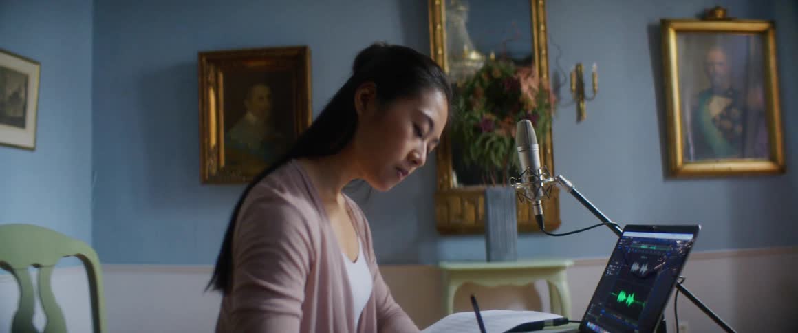A young woman at home sits in front of her computer and writes music