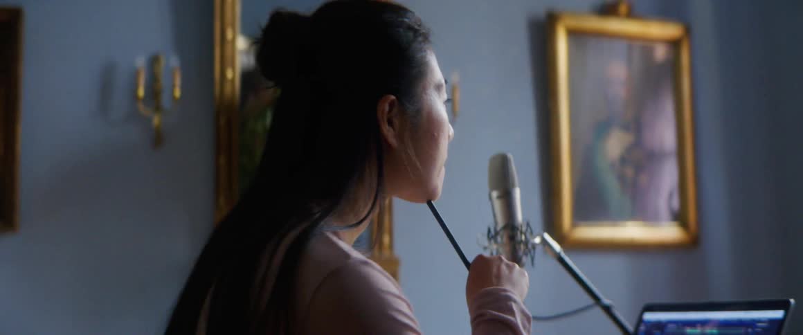 Woman writes on paper near microphone and laptop showing audio display