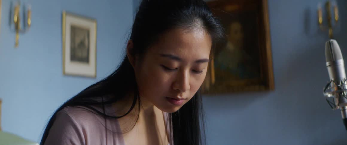A young woman sitting at a table writes notes on a music sheet