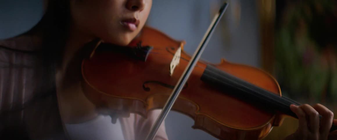 Woman plays violin near blue wall decorated with gold framed art
