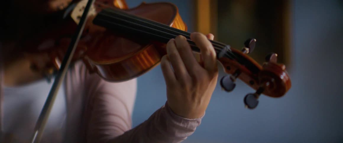 Asian woman holding a violin against her neck and moving a bow plays a violin