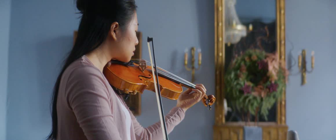 A teenage girl playing the violin at home