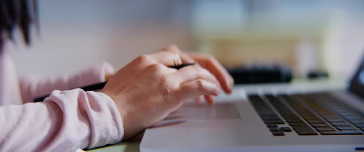 Woman types on laptop holding pencil