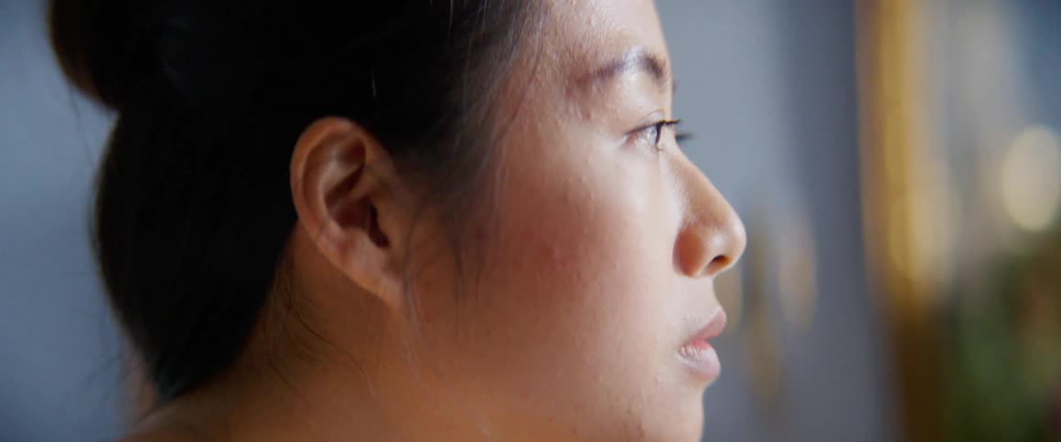 A young woman at home looks around the room as she thinks