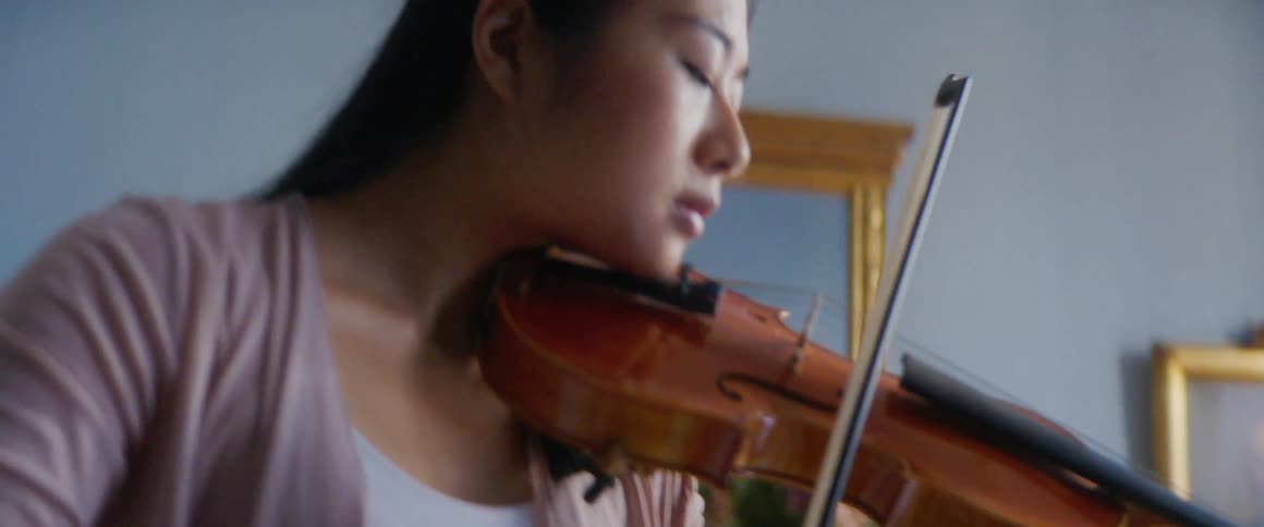 A young woman plays the violin in the room of a house during the day