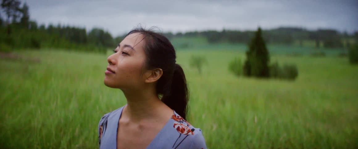 A woman smiles as the wind blows through her hair while standing in a meadow